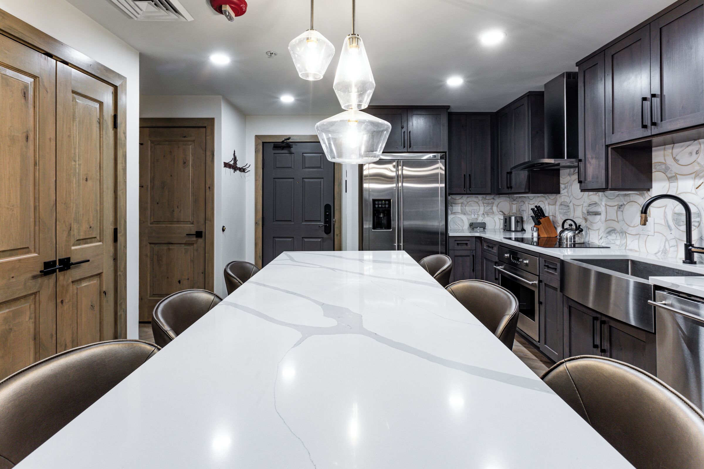 A modern kitchen with a large island, stainless steel appliances, and dark wooden cabinets.