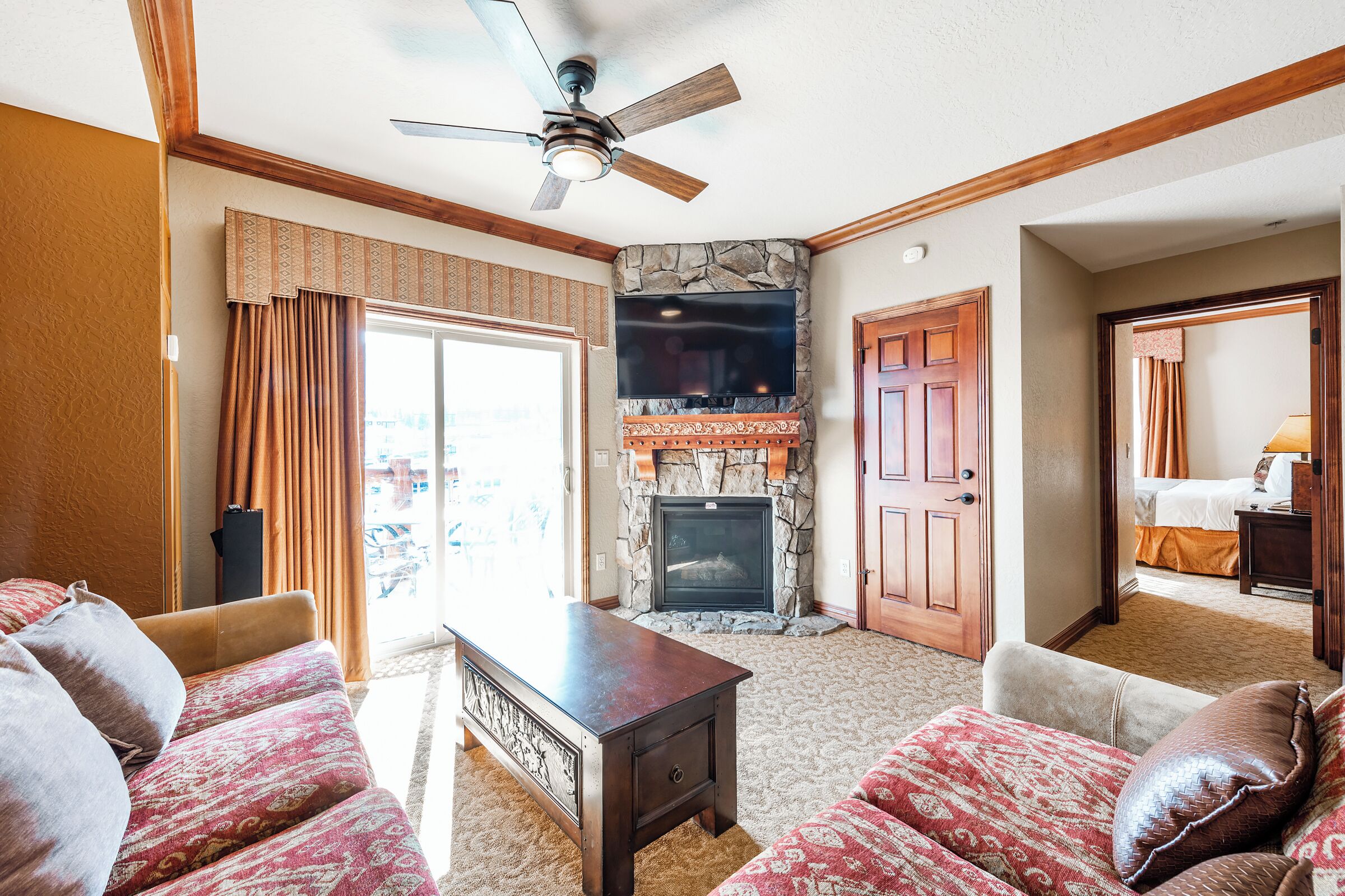 Habitación de hotel con chimenea, televisión, ventilador de techo y un amplio ventanal con cortinas.