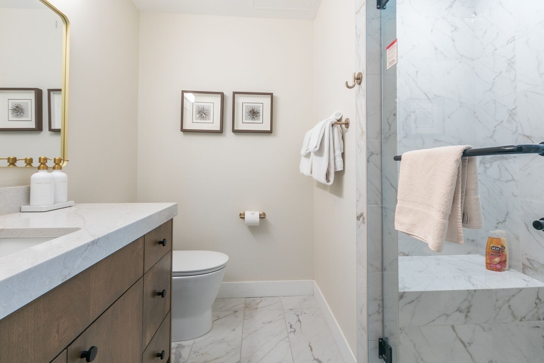 A bathroom with a marble floor, a toilet, a sink with gold fixtures, and a shower with a glass door.