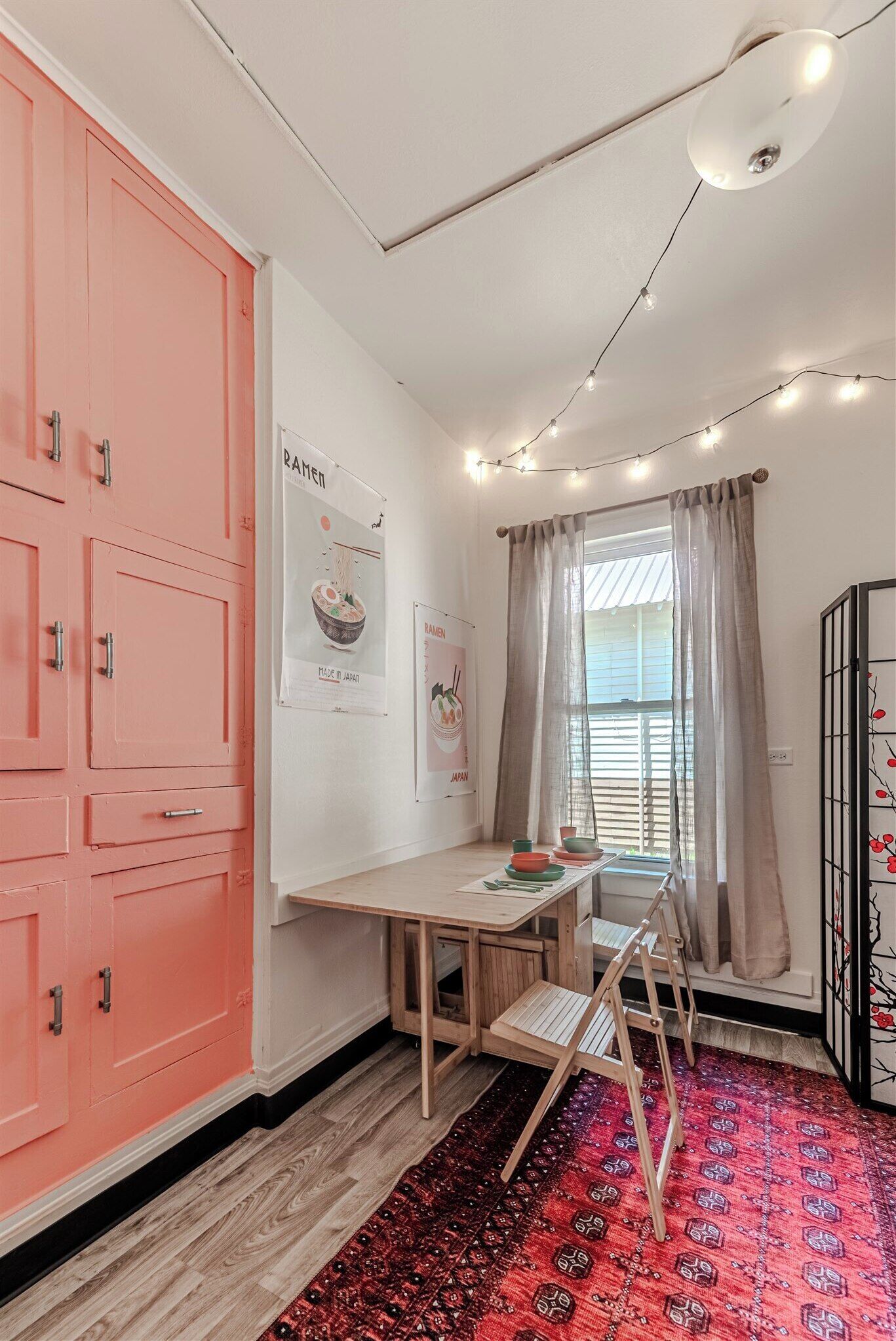Une pièce de taille modeste, avec un meuble rose, un bureau en bois, une échelle et une fenêtre avec des rideaux.