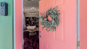 Une porte rose ornée d’une guirlande, une bibliothèque en arrière-plan et une guirlande lumineuse.