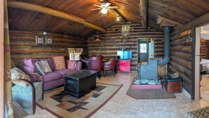 A log cabin interior with a sofa, chairs, a coffee table, a fireplace, and a television.