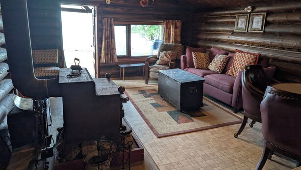 A rustic cabin interior with a wooden ceiling, a sofa, a table, and a fireplace.