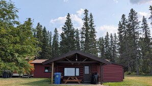 A red cabin with a wooden deck, a picnic table, and a blue trash bin.