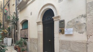 A narrow street with a building featuring a black door, potted plants, and a sign indicating a hotel. - Dimora San Triggiano (Bari)