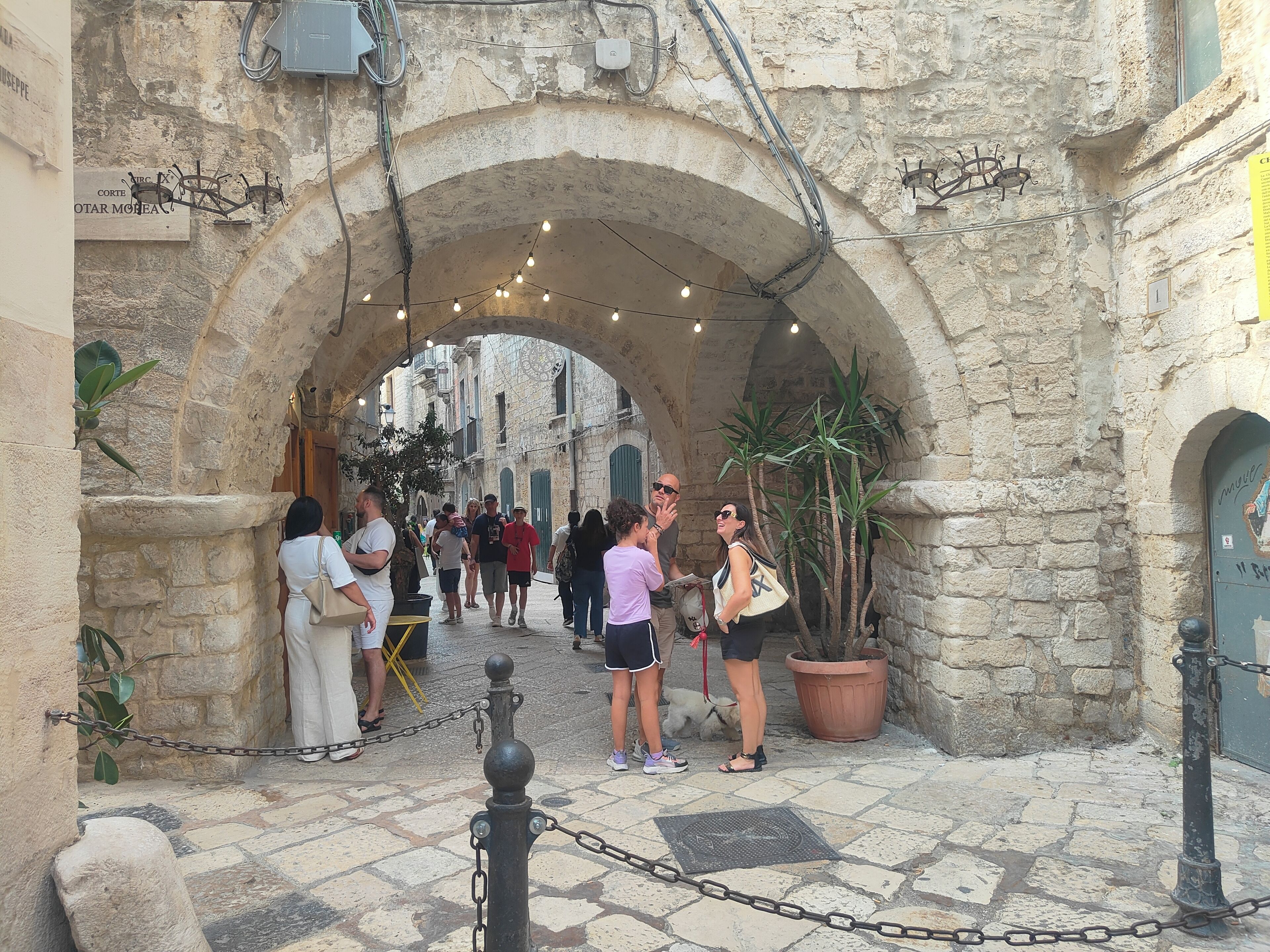 A stone archway in a historic town square with tourists walking through.