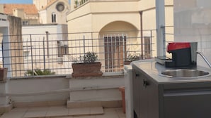 A balcony with a sink, a potted plant, and a view of a building with a clock tower. - Dimora San Triggiano (Bari)