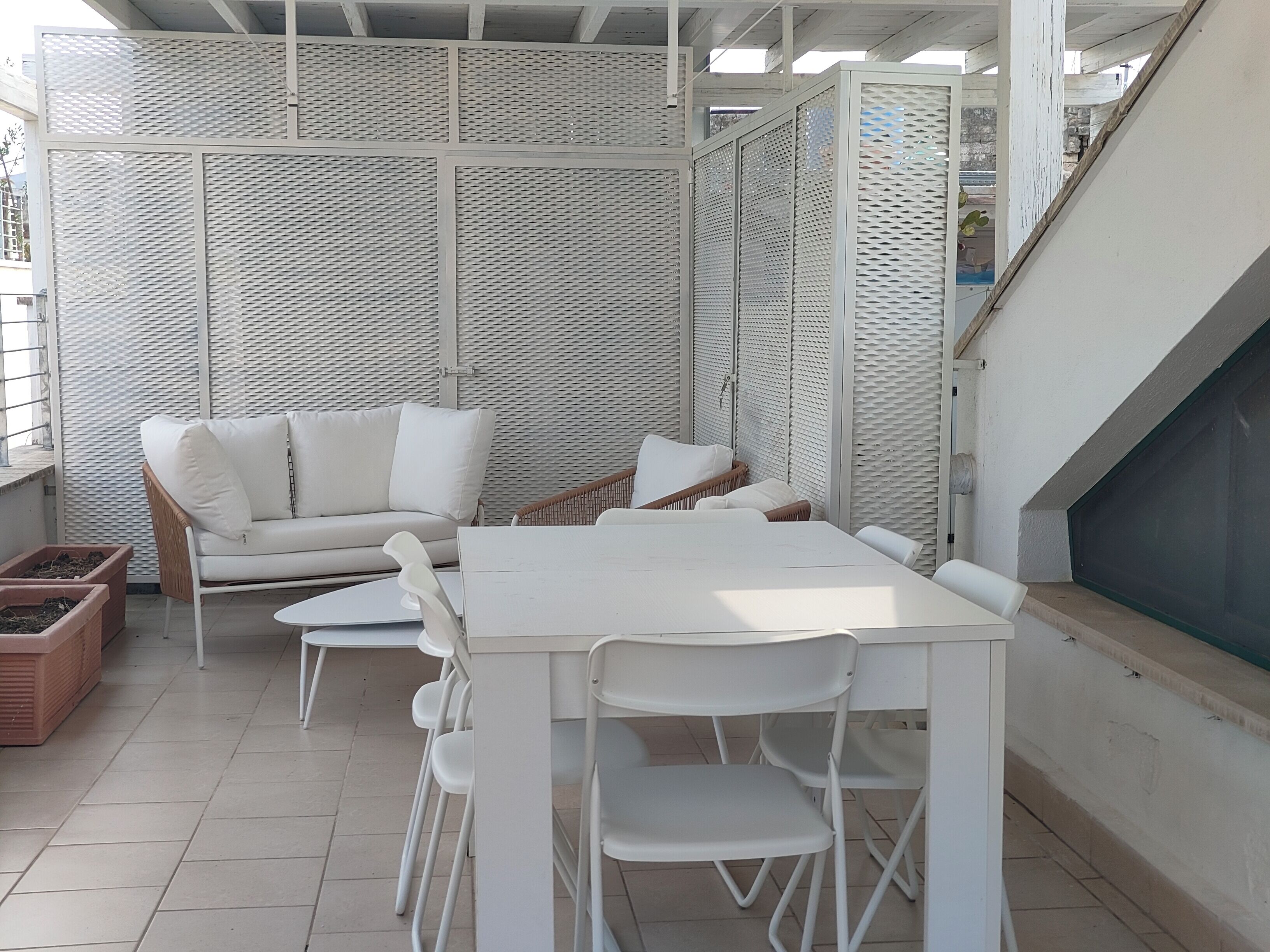 Un patio con una mesa y sillas blancas, un sofá blanco y una silla de mimbre.