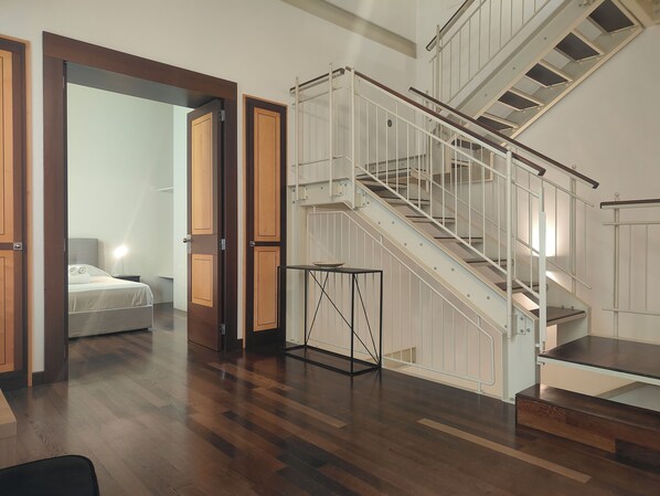 A modern interior with a wooden floor, a staircase with white railings, and a bed in the background.