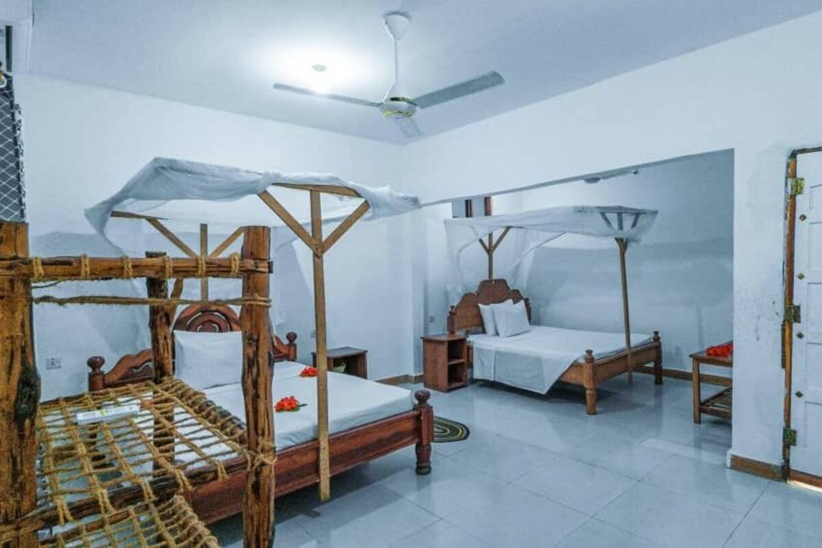 Una habitación con tres camas de madera, cada una con dosel, y un ventilador de techo.