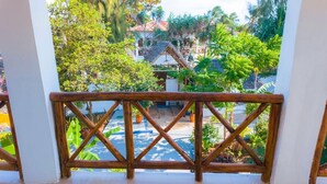 A wooden balcony railing overlooking a garden with a thatched-roof structure and lush greenery. - Green House Zanzibar (Nungwi)