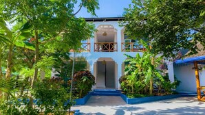 A traditional building with a central entrance, surrounded by lush greenery and a blue pathway. - Green House Zanzibar (Nungwi)
