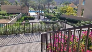 A resort with a pool, palm trees, and a mountainous backdrop. -  Two Bedroom Apartment Muscat Bay (Bandar Jissah)
