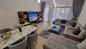 A modern living room with a sofa set, a dining table, and a TV. -  Two Bedroom Apartment Muscat Bay (Bandar Jissah)