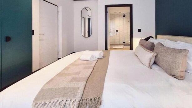 A modern hotel room with a large bed, a walk-in shower, and a view of the city.