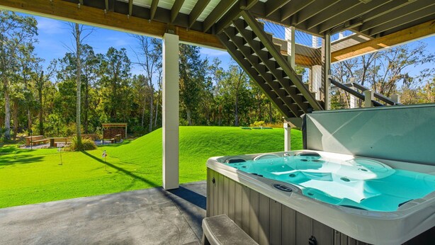 Un jacuzzi bajo un porche cubierto con vistas a un césped cuidado y árboles.