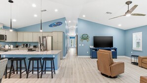Una cocina moderna con una isla central, taburetes de bar y un televisor de pantalla plana sobre un pedestal.