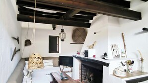 A rustic room with a wooden ceiling, a fireplace, a bed, a table, and various decorative items.