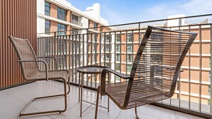 Un balcon avec deux chaises à ossature métallique et une petite table, donnant sur un immeuble moderne doté de grandes fenêtres.