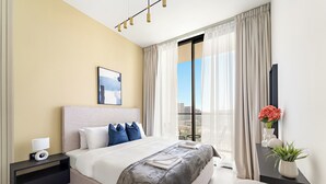 Une chambre d’hôtel moderne avec un grand lit, une table de chevet avec une lampe, une petite table ornée d’un vase de fleurs et une vue sur la ville par la fenêtre.