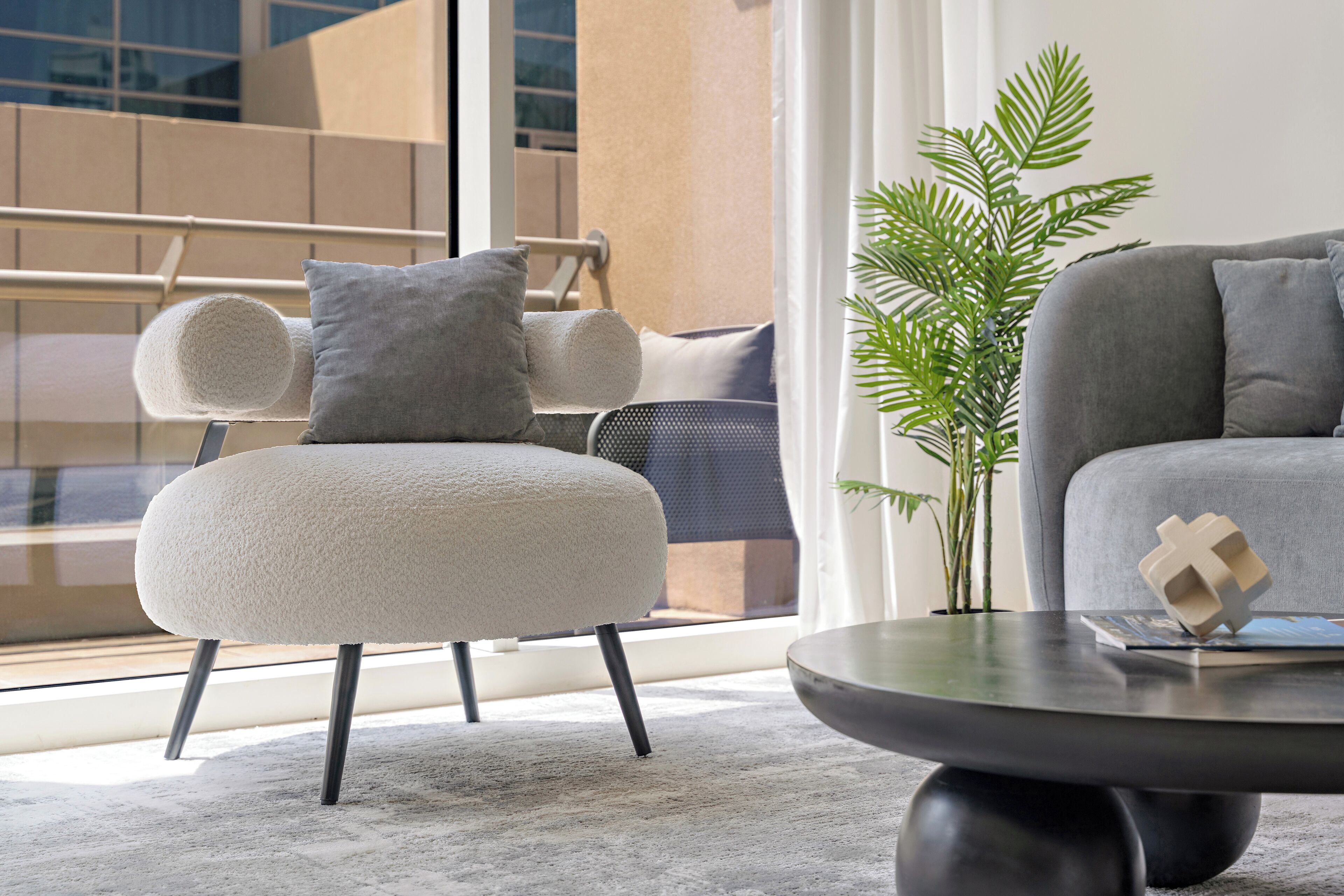 Ein modernes Wohnzimmer mit einem runden Couchtisch, einem grauen Sofa und einem weißen Sessel mit grauem Kissen.