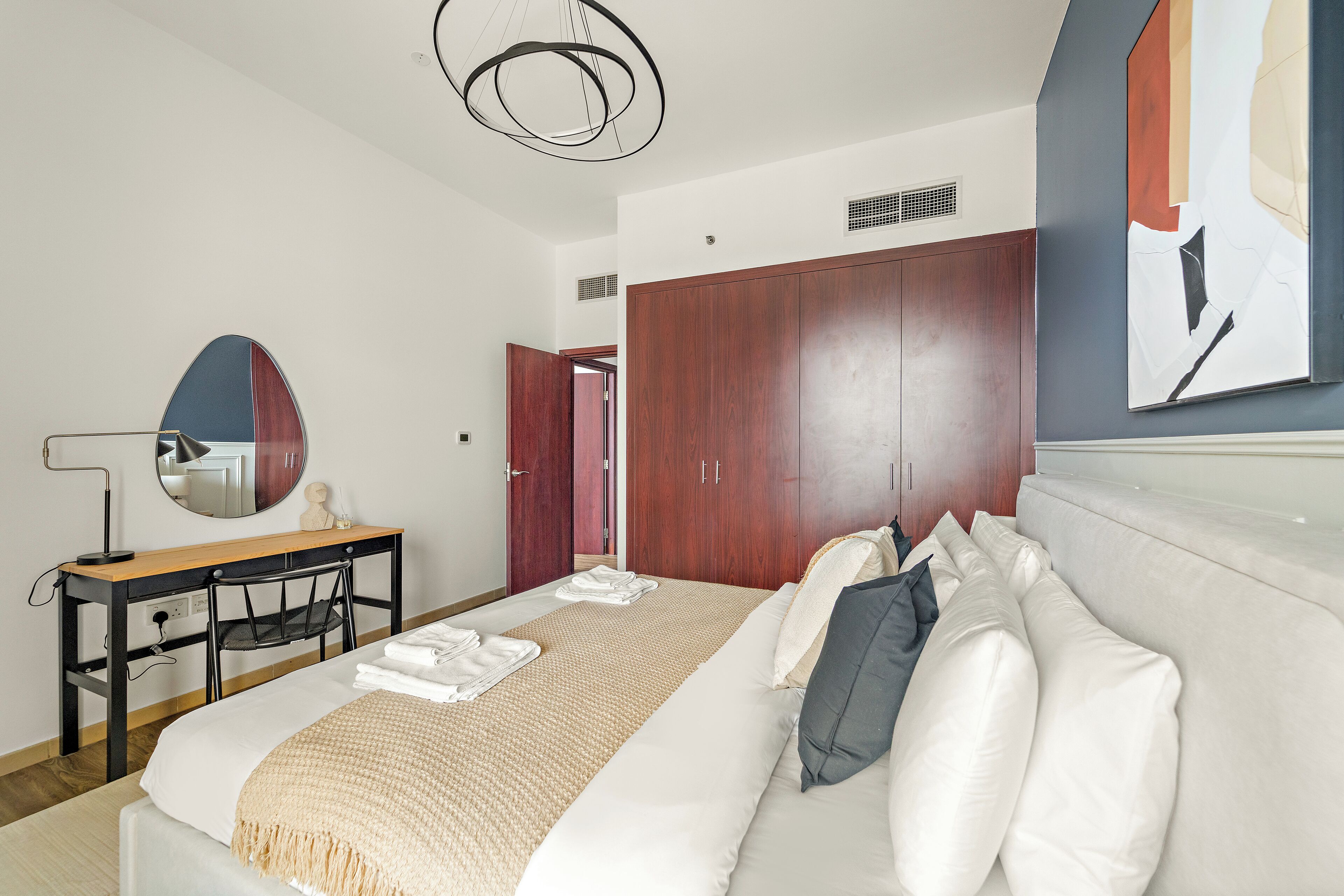 Una habitación de hotel moderna con una cama grande, un escritorio con espejo y un armario.