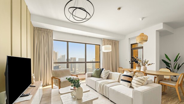 A modern living room with a large sofa, a dining table, and a TV. - Silkhaus Amwaj 4 (Dubai)