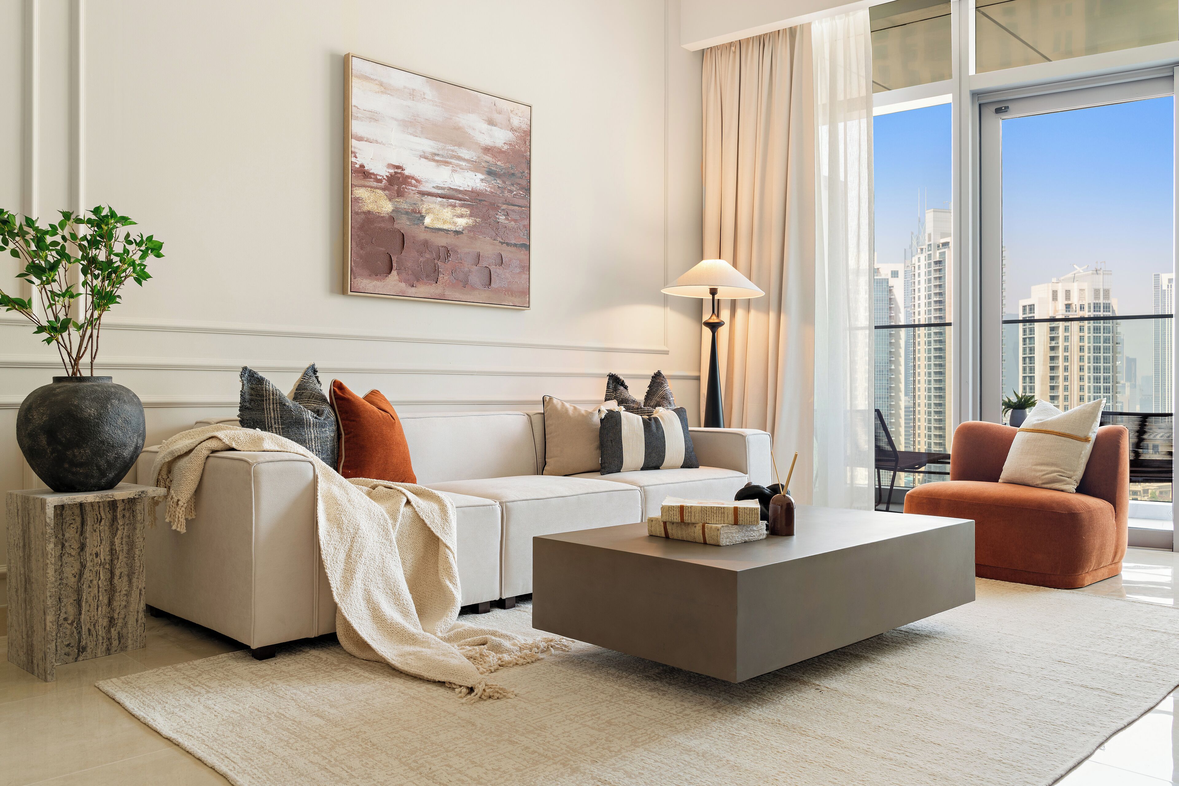 A modern living room with a sofa, coffee table, and a view of the cityscape through large windows.