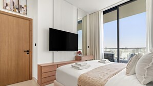 Een moderne hotelkamer met een groot bed, een flatscreen televisie aan de muur, een houten garderobe en uitzicht over de stad door grote ramen.