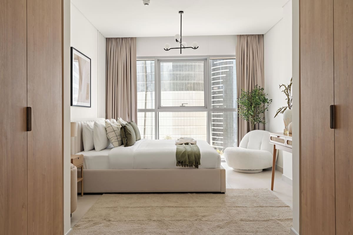 A modern bedroom with a large bed, a desk, and a window with curtains.