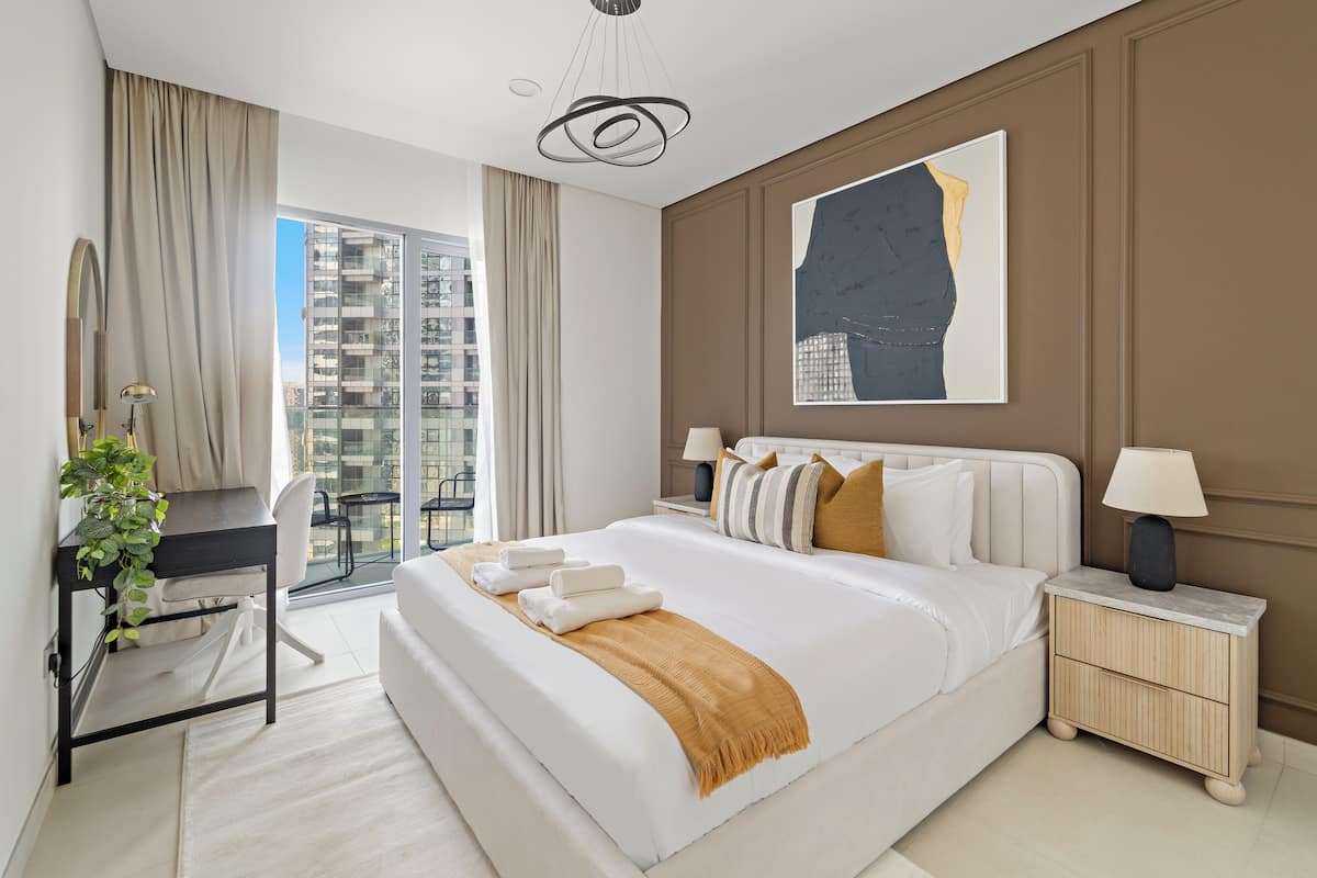 A modern hotel room with a large bed, a desk, and a view of a high-rise building.