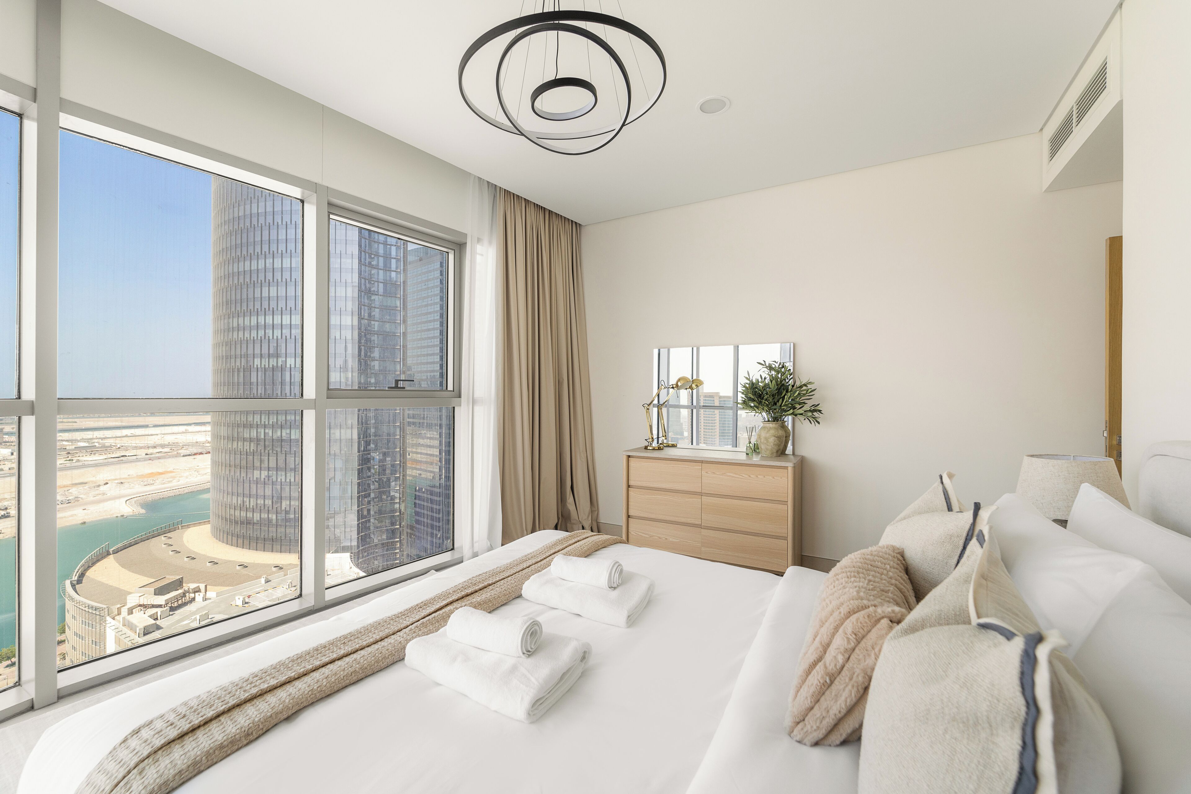 A modern hotel room with a large window offering a view of a cityscape and water.