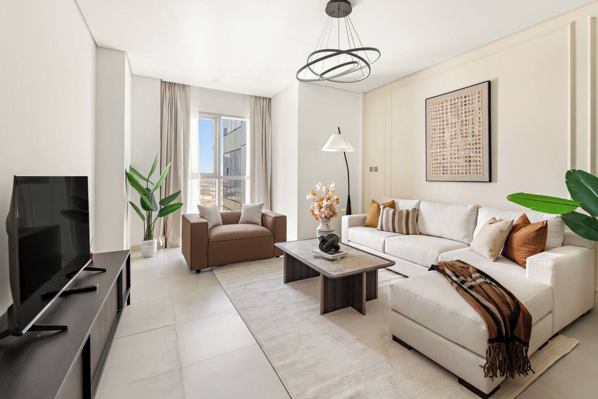 A modern living room with a flat-screen TV, a sofa, a coffee table, and a potted plant.