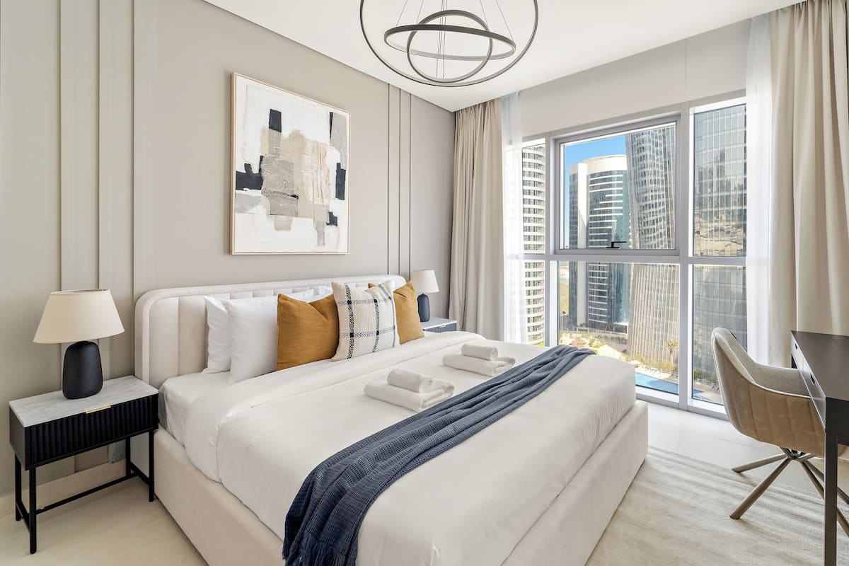 A modern hotel room with a large bed, a desk, and a view of tall buildings.