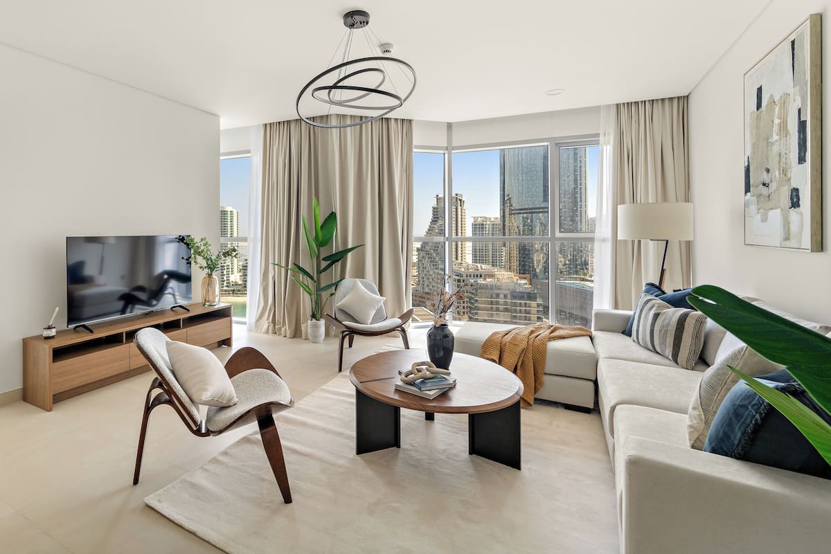 A modern living room with a large TV, comfortable seating, a coffee table, and a view of the city.