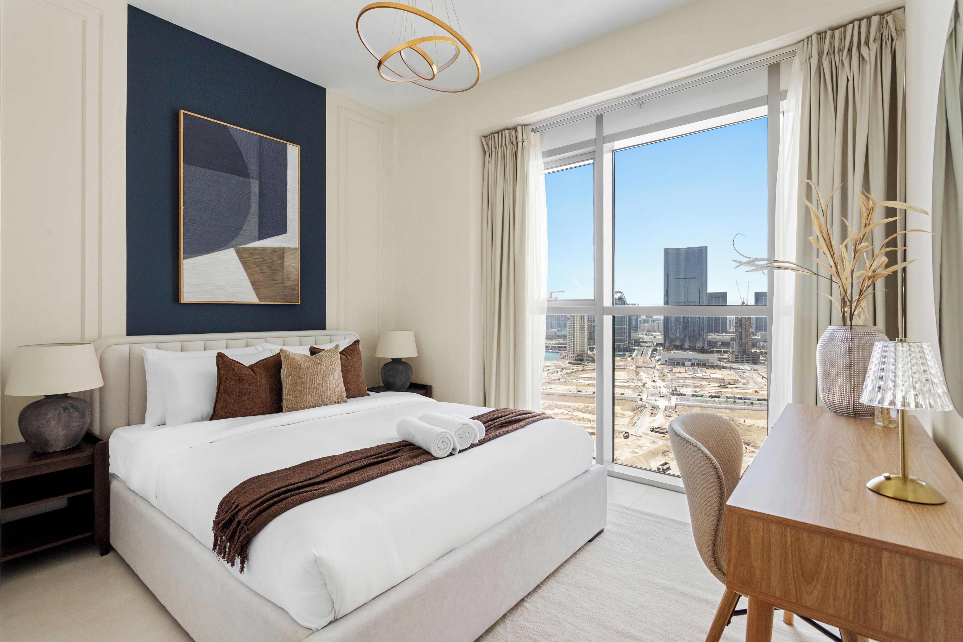 Ett hotellrum med en stor säng, ett skrivbord, utsikt över staden och en modern, abstrakt målning på väggen.