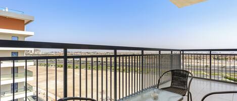 A balcony with a table and chairs, overlooking a parking area and buildings.