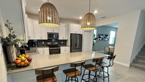 Una cocina moderna con armarios blancos, una isla grande con taburetes altos y dos lámparas colgantes.
