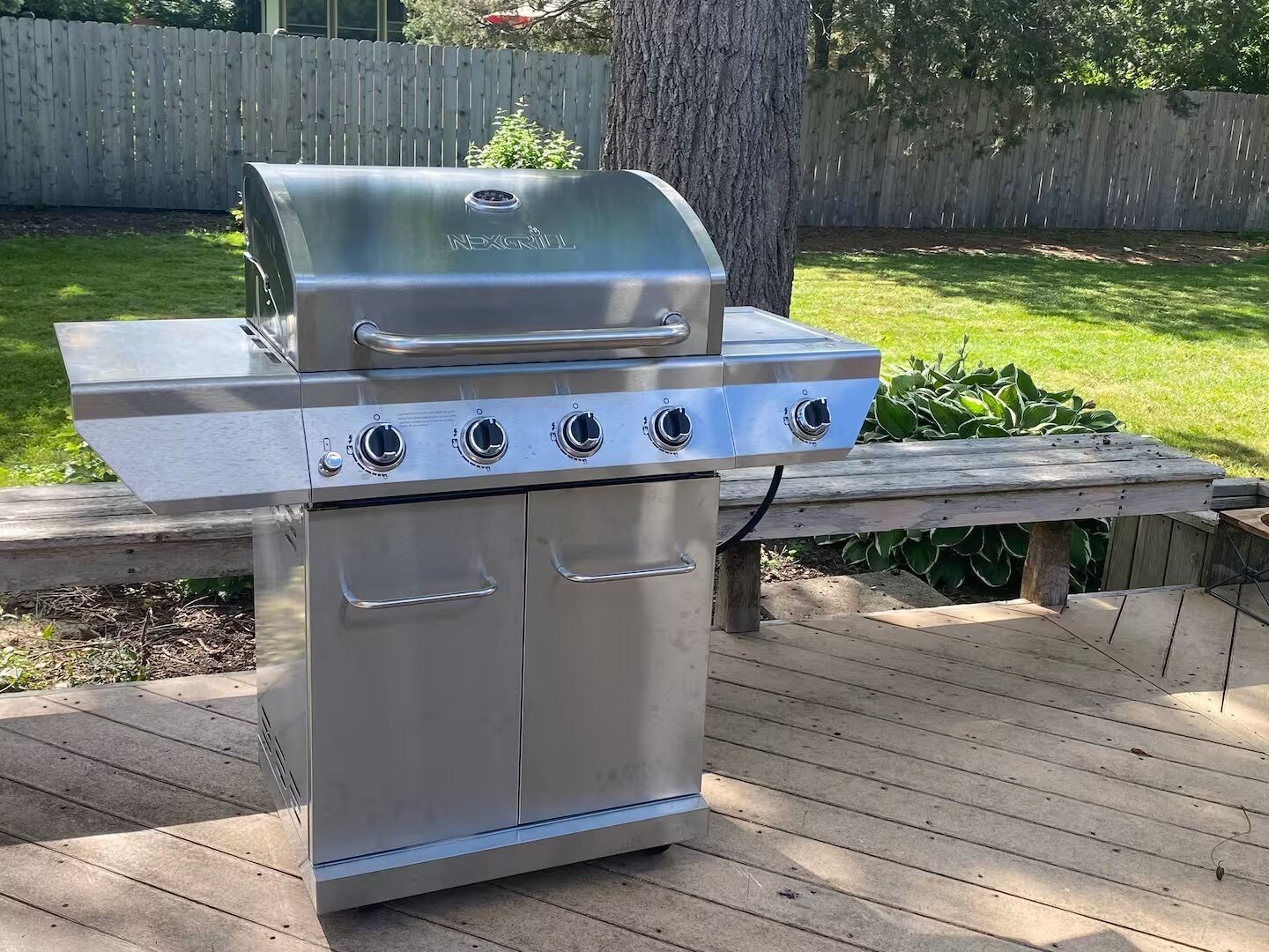 A stainless steel outdoor grill with four burners and a lid, placed on a wooden deck.