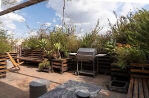Un espace extérieur aménagé en terrasse, avec des meubles en bois, un barbecue et diverses plantes en pot.