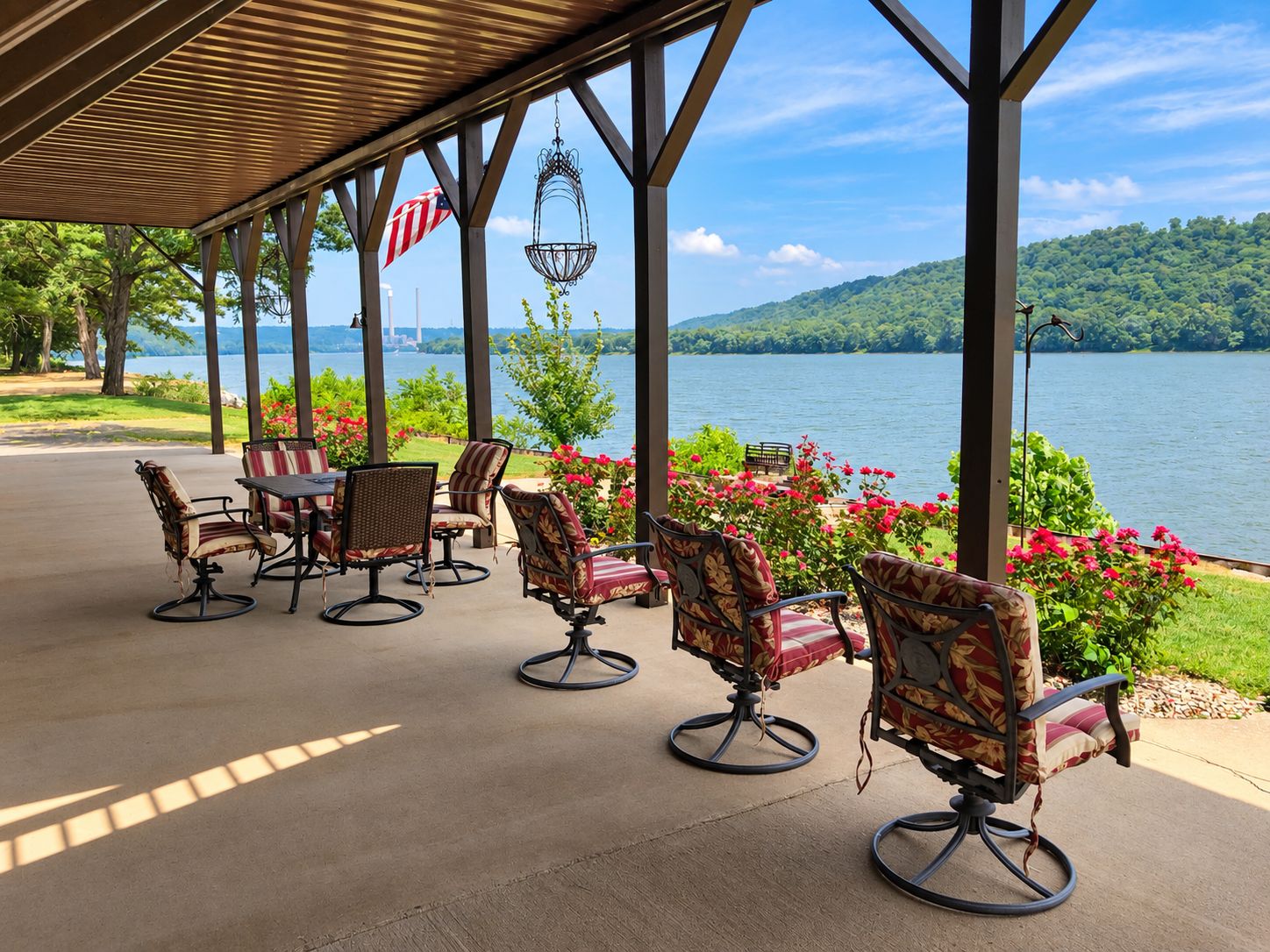 Une terrasse extérieure donnant sur un lac, avec une table et des chaises, un drapeau américain et un luminaire suspendu.