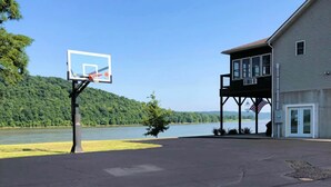 A basketball court with a hoop, a building with a balcony overlooking a lake, and an American flag. - T&E Riverhouse Retreat (Hanover)