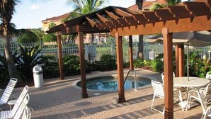 A pool area with a pergola, lounge chairs, and a small table. - Gardens of Beachwalk 1/1 with Balcony (Fort Myers)