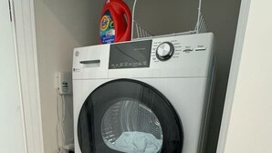 Una lavadora y secadora apiladas en un cuarto de lavado, con una botella de detergente encima.