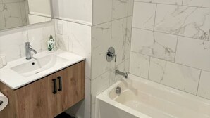 Un baño moderno con lavamanos blanco, tocador de madera, bañera y ducha con puerta de vidrio.