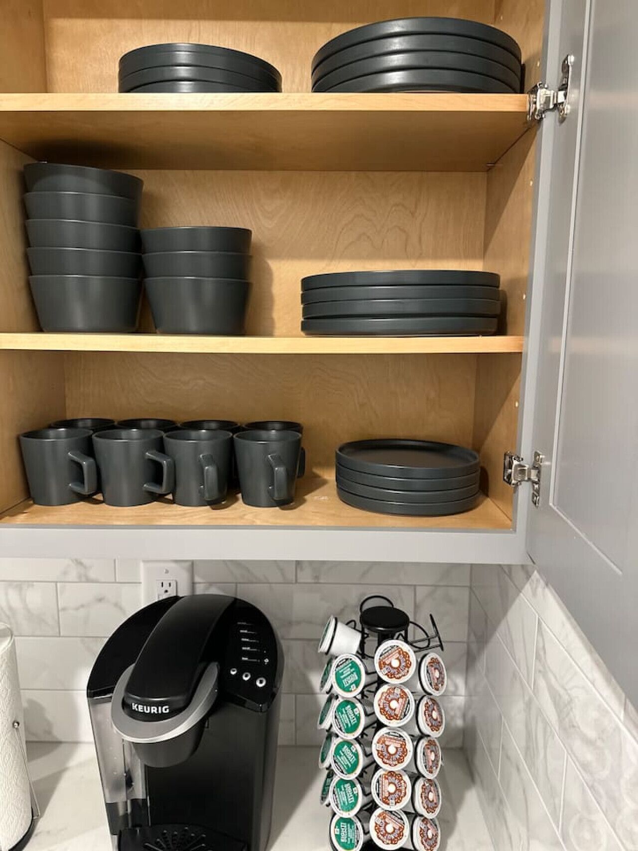 Una cocina con estantes de madera que sostienen ollas y sartenes negras, una cafetera y un dispensador de cápsulas de café.
