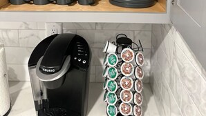 Une cuisine avec des étagères en bois où sont rangées des casseroles et des poêles noires, une machine à café et un support à capsules de café.
