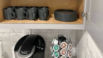 Una cocina con estantes de madera que sostienen ollas y sartenes negras, una cafetera y un dispensador de cápsulas de café.