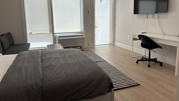 Une chambre à coucher moderne, dotée d’un grand lit, d’un bureau, d’une chaise et d’un téléviseur fixé au mur.