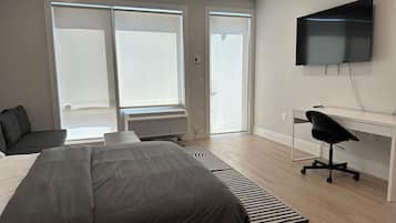 Un dormitorio moderno con una cama grande, un escritorio, una silla y un televisor montado en la pared.